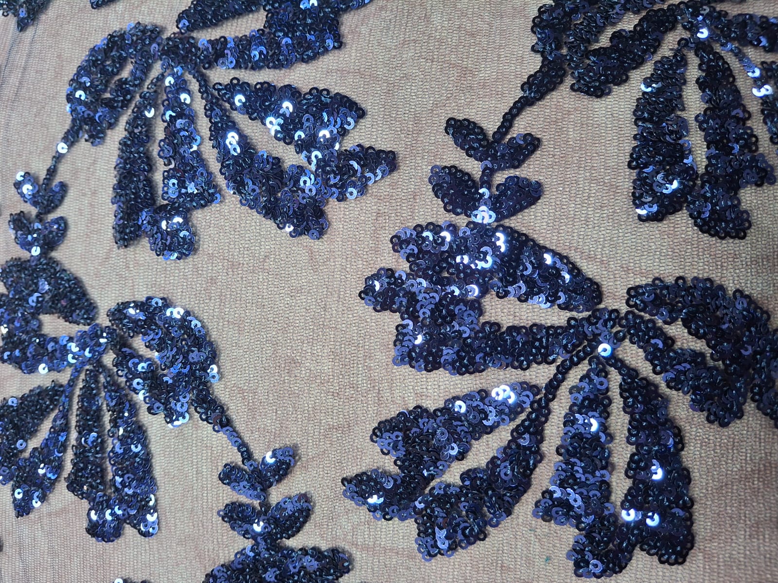 Primer plano de tela clara con lentejuelas azules en motivos de hojas
