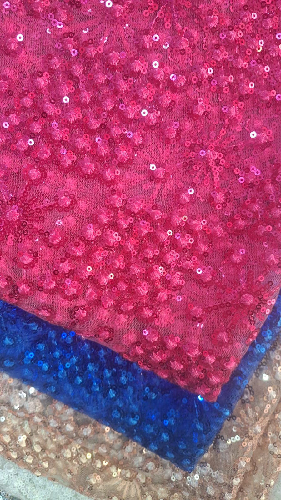 Primer plano de lentejuelas rosadas con bordado floral sobre tela fucsia, con telas azules y claras debajo