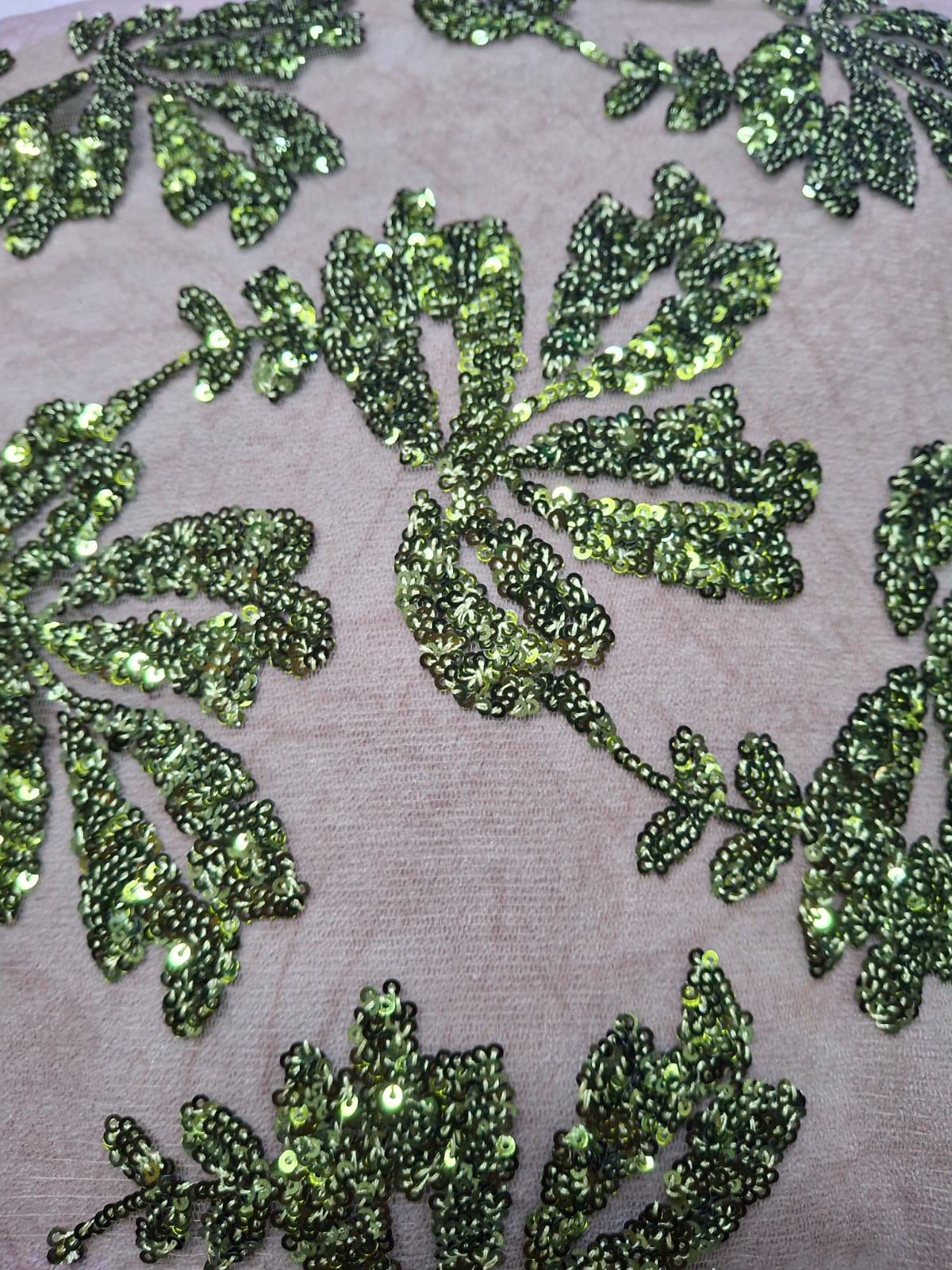 Primer plano de tela clara con lentejuelas verdes en motivos de hojas