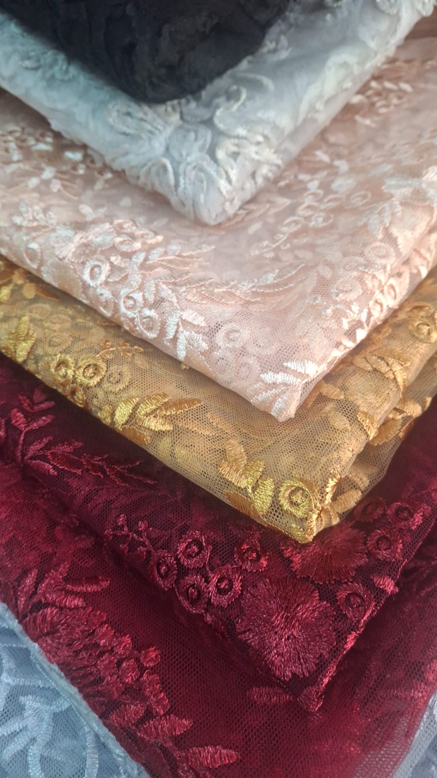 Capas de encajes bordados apilados en rosa perla, dorado, vino y negro